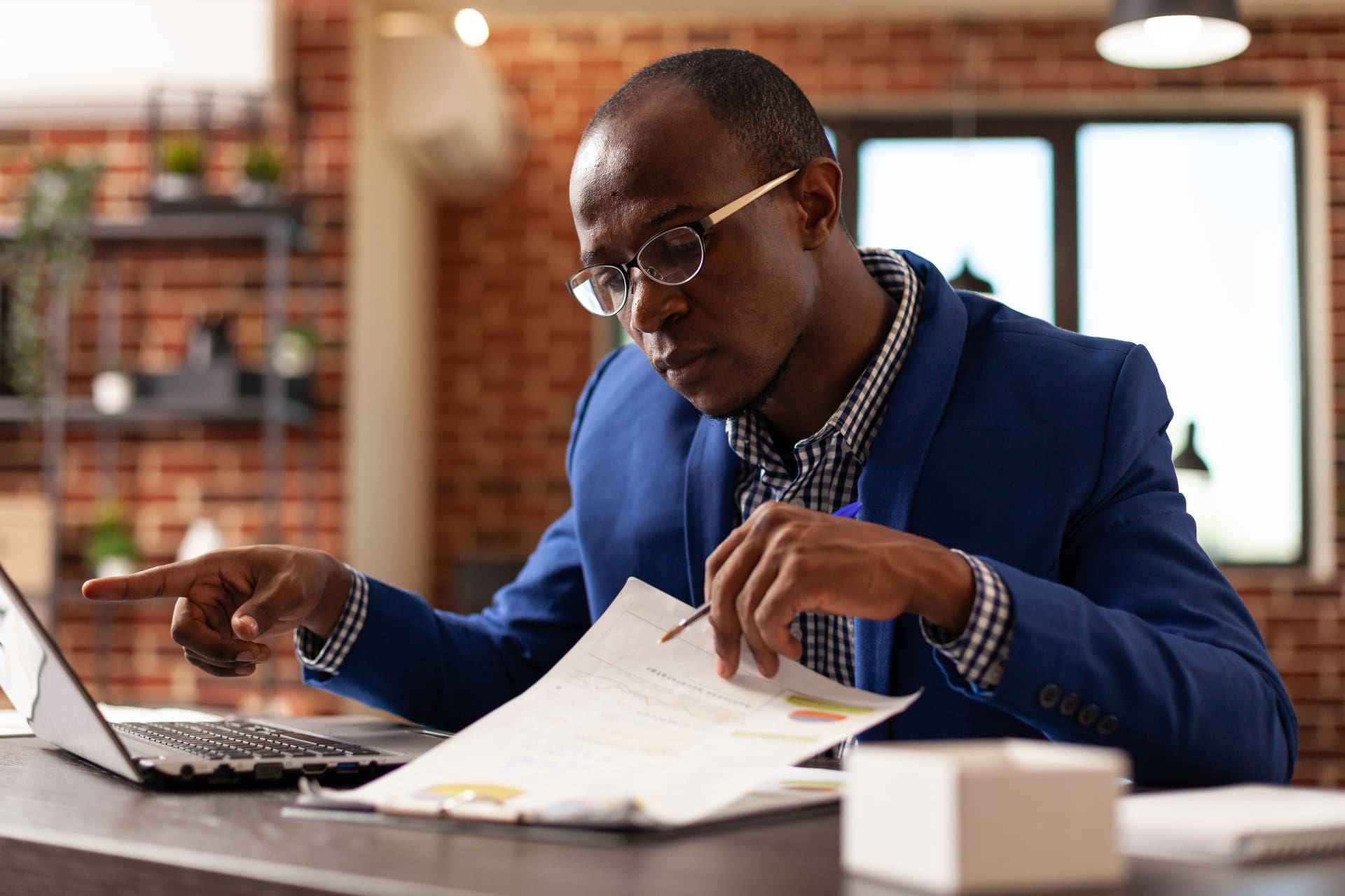 Business man analyzing papers on clipboard to plan marketing strategy with laptop. Entrepreneur using computer and financial documents to work on project planning in startup office.